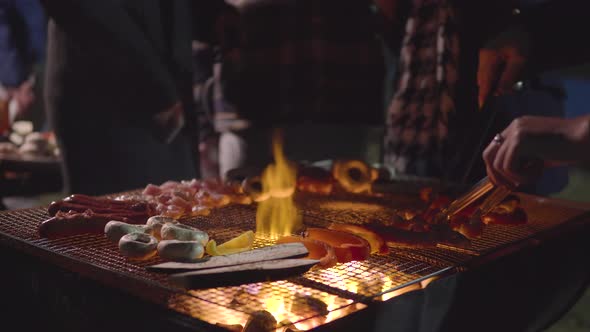 People standing in front of the BBQ and grilling mushrooms, sausage, chicken, eggplant in front of t