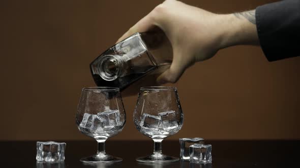 Pouring Whiskey, Cognac Into Glass. Brown Background. Pour of Alcohol Drink