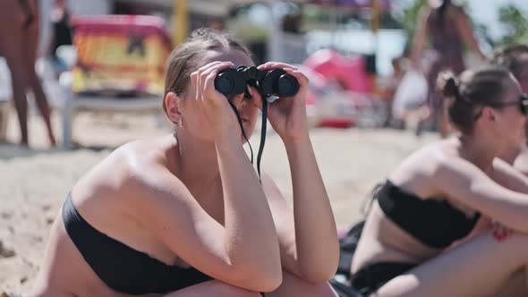 Beautiful Girl Looks Through Binoculars on the Beach