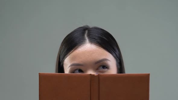 Asian Female Student Hiding Behind Book, Education in University, Close-Up