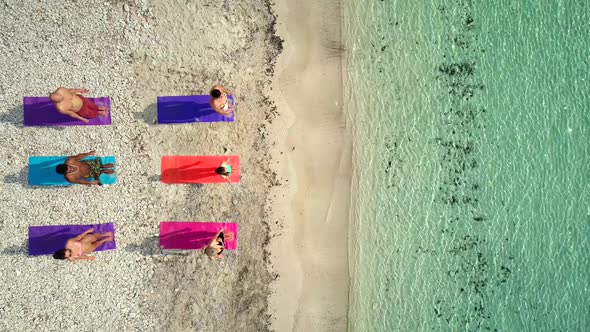 Aerial view of group of people doing yoga on colorful mats on sandy beach.