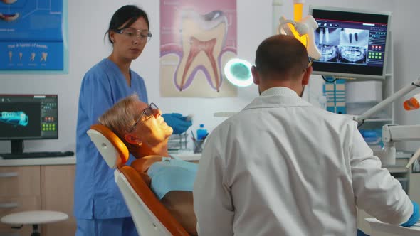 Dentist Working in Dental Unit with Nurse and Man Lying Patient