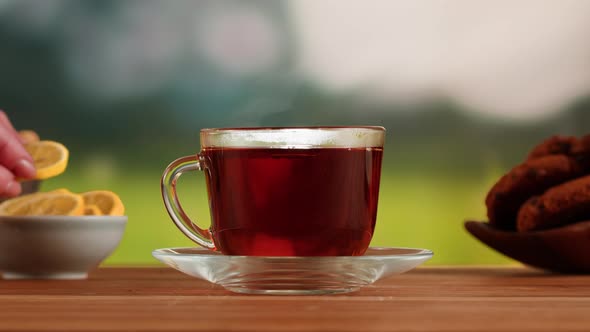 Putting Orange Into Black Tea in Cup on a Wooden Table