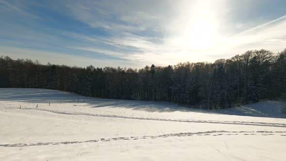 Timelapse of a backlit winter scene. Moving clouds over a valley of white snow framed by a nearby fo