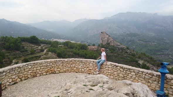 Woman Sitting and Looking at a Beautiful View with a Blue Lake and Mountains From the Wall of an Old