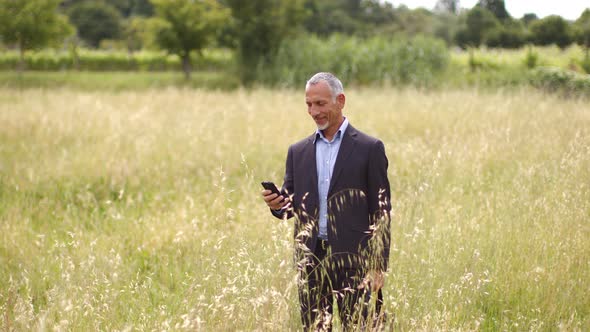 Smiling businessman standing in meadow reading text message