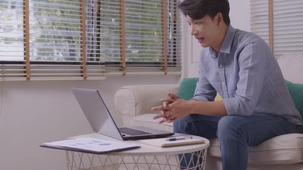 At home, an Asian businessman works on a desk with a laptop, searching for jobs and paperwork.