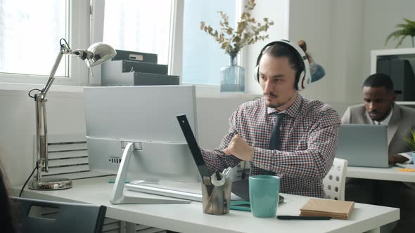 Creative Young Man in Headphones Dancing Working with Computer at Desk in Office