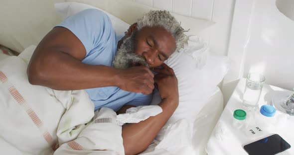 Senior man with tissue coughing in the bed at home