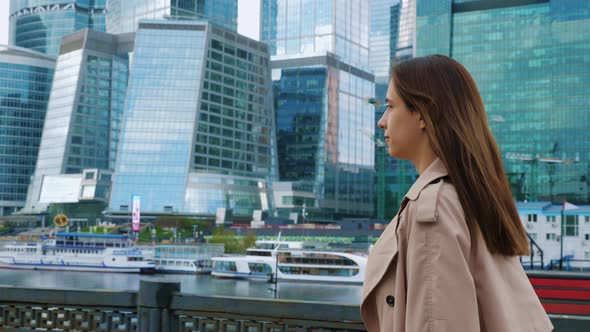 Brownhaired Woman Walks at Street in City Near Skyscrapers