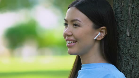 Pretty Woman Listening to Music Through Wireless Earbuds, Relaxing in Park