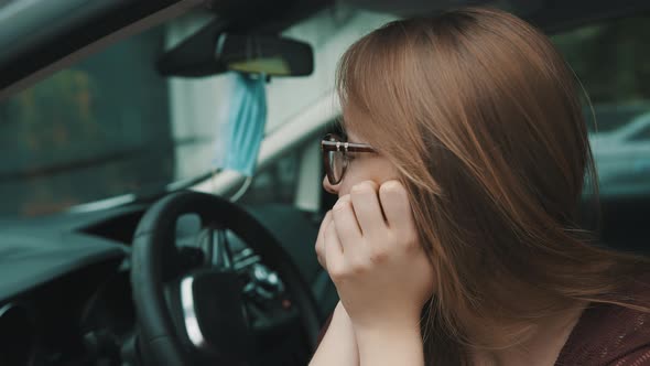 Close Up, Face Expression of Young Caucasian Woman Sitting on the Driver Seat. Face Mask Hanging on