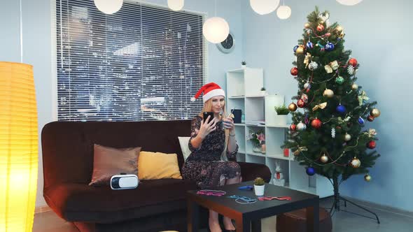 Attractive Young Lady Making Selfie in Santa Hat and with Drink in Her Hands