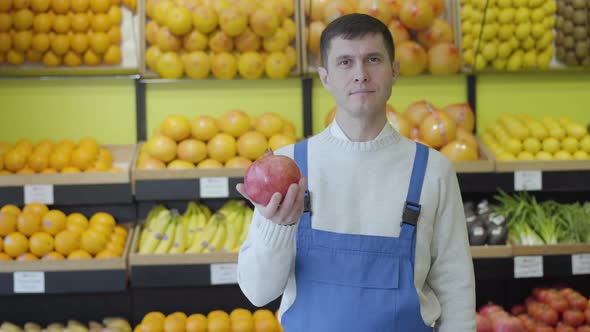 Portrait of Positive Caucasian Brunette Man in Uniform Holding Pomegranate and Showing Thumb Up at