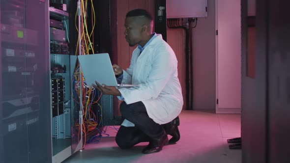 African american male computer technician using laptop working in business server room