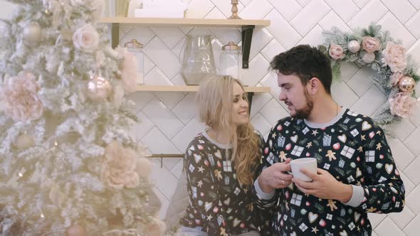 Attractive Cheerful Man and Woman Sitting Near Christmas Tree Hugging