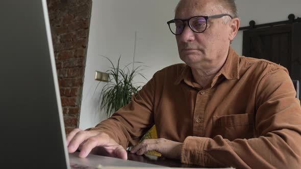 Old man in eyeglasses using laptop computer at home.