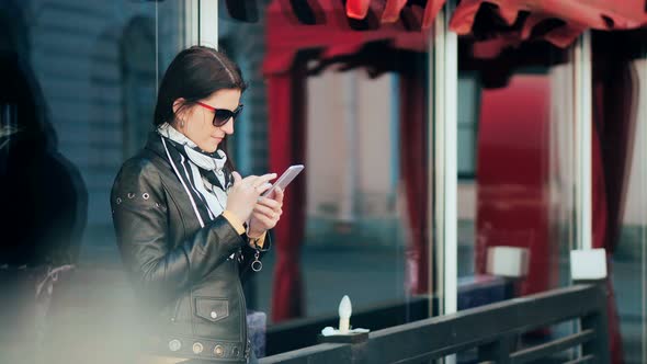 Beautiful Young Brunette Woman Messaging on the Smartphone at the City Street Background