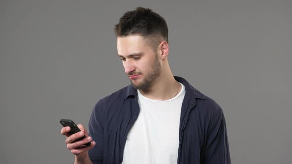Portrait of Modern Guy with Beard in Casual Tshirt Browsing Internet on Smartphone and Finding Good