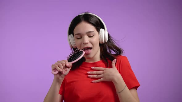 Young Pretty Woman Singing and Dancing with Hair Brush or Comb Instead Microphone at Violet Wall