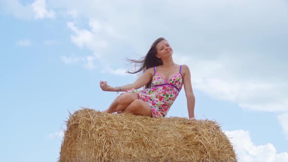 Woman Sitting on Hay Ball on Background of Blue Sky with White Clouds