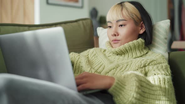 Confident Asian woman typing at laptop at home