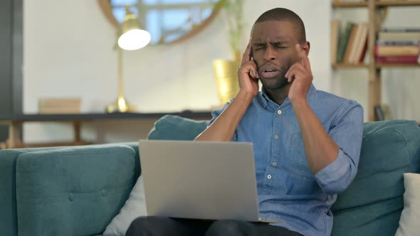 Young African Man with Laptop Having Headache on Sofa 