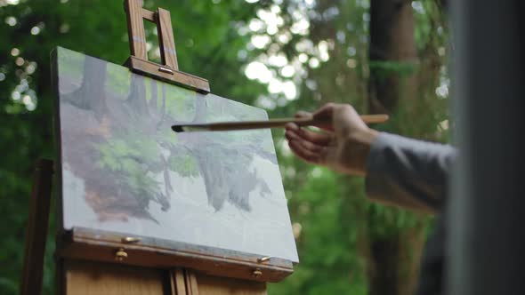 Girl with a Brush in Her Hands Paints a Lake and Trees on Canvas on Tripod.