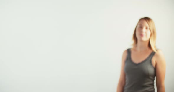 Young blond woman walking up to the camera and smiling on white studio background