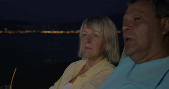 Senior couple relaxing with cocktails on beach at night