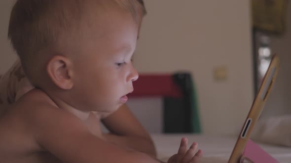 Two Kids in Bed Playing a Tablet in Social Internet in the Dark Light. Close Up of Little Boy and