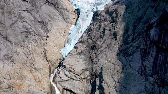 Glacier melting and forming a waterfall through a rocky mountain - Aerial footage