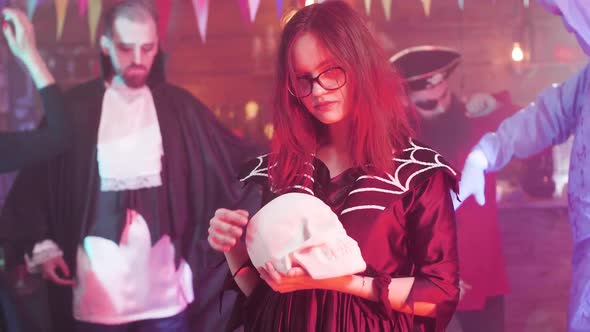 Young Girl in Eyeglasses Disguised As a Witch and Holds a Skull in Her Hands