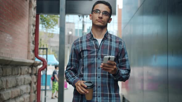 Portrait of Attractive Middle Eastern Man Walking Outdoors Drinking to Go Coffee and Using