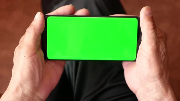 In the hands of the old man a smartphone with a green screen