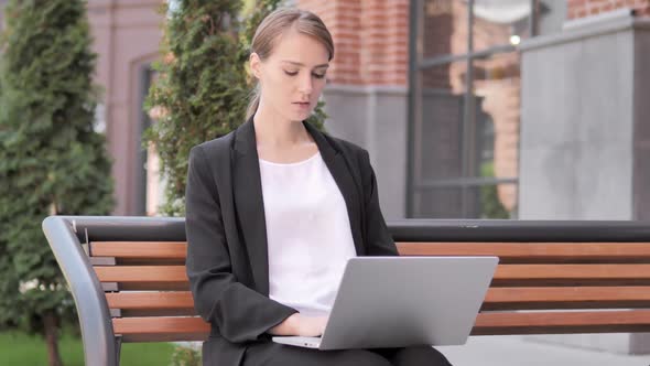 Young Businesswoman Working on Laptop Sitting Outdoor on Bench