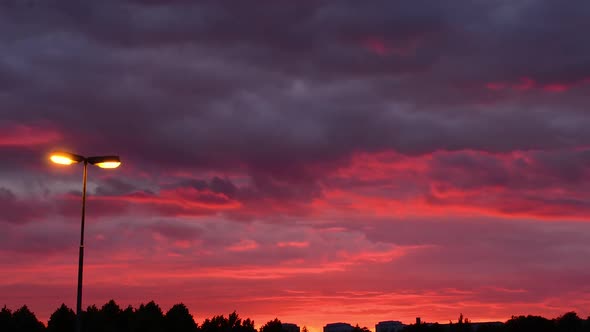 Sunset timelapse in summer, deep red sky and fasting clouds with buildings in horizon and streep lam