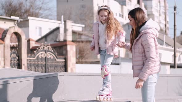 The Woman Is Helping the Child Go Roller-skating in a Skate Park Outside