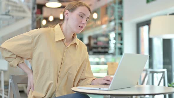 Young Woman with Back Pain Using Laptop in Cafe