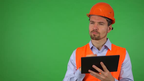 A Young Handsome Construction Worker Works on a Tablet - Green Screen Studio