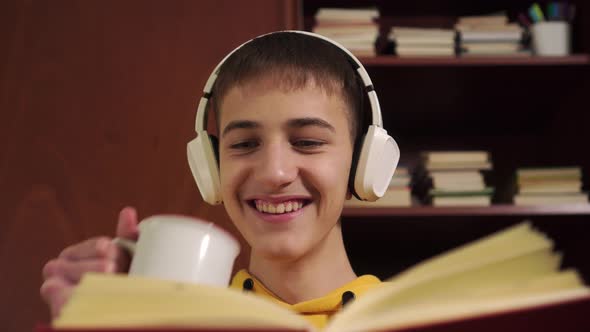 Happy Laughing young student reads a book in headphones 