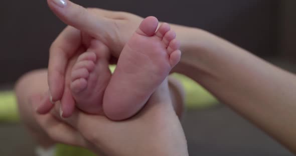 Mom's Hands Holds and Caresses Baby's Cute Feet at Camera