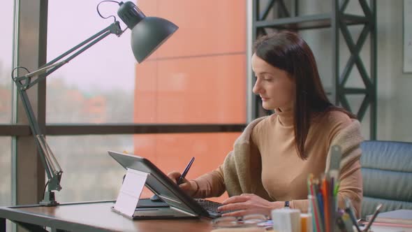 A Professional Designer in the Office Draws with a Stylus on a Graphic Tablet Sitting in an Office