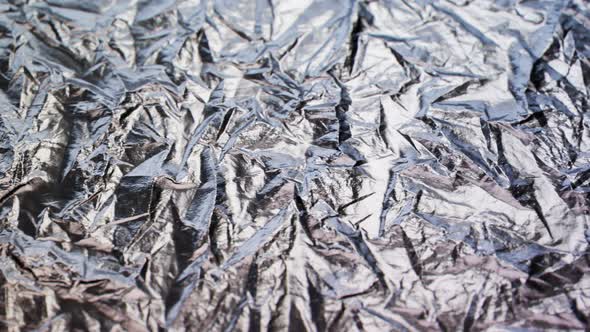 Crumpled, aluminium foil shining in the spotlight. Endless, abstract pattern. 4K