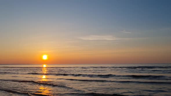 Picturesque sunset on the sea or ocean. Waves roll on the shore in the sun