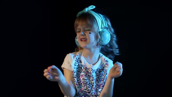 Stylish Teenager Kid Girl Standing Among Neon Lights Listening To Music in Headphones Dancing