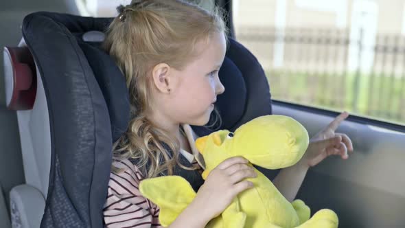 Little Girl Traveling in Car with Toy alt