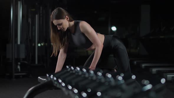 Young Woman in the Gym Girl Lifts a Dumbbell in a Tilt Muscle Training with Weights