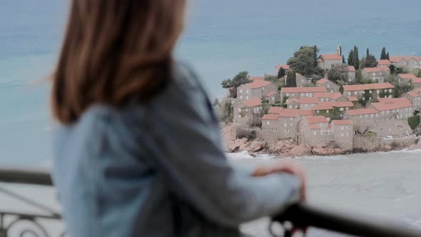 Young woman in a beige sweater stands on the balcony. Wind develops female’s hair, freedom concept