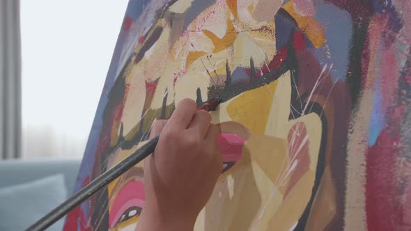 Close Up Of A Hand Holding Paintbrush Mixed Colour And Painting A Girl's Face On The Canvas